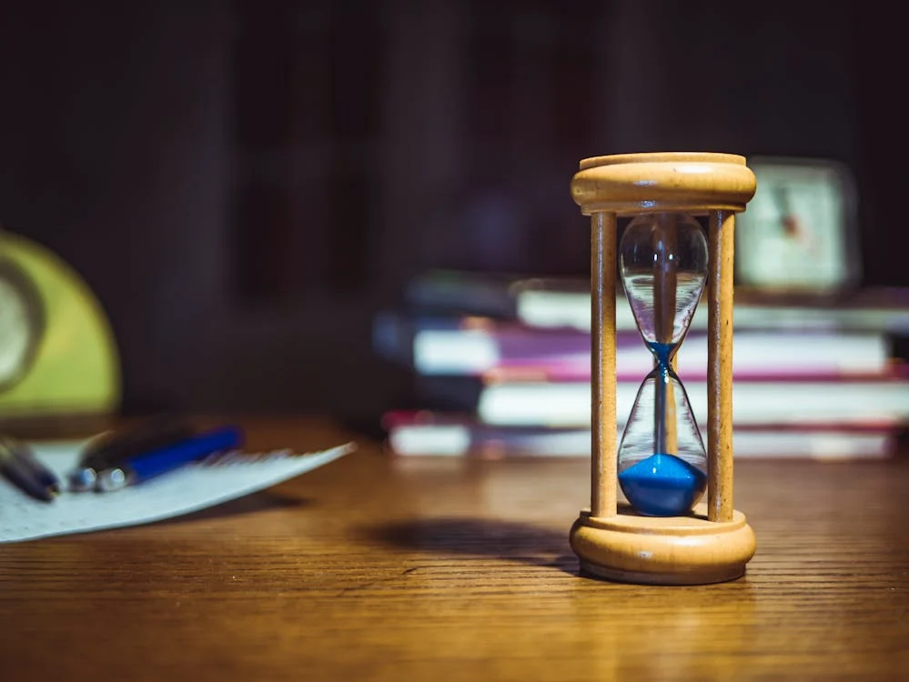 hourglass on wooden table with study materials in background