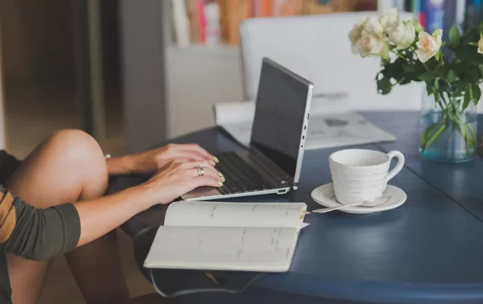 person working on laptop next to open notebook and coffee cup