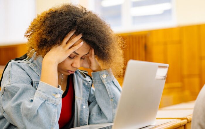 woman holding head with eyes closed while seated in front of laptop