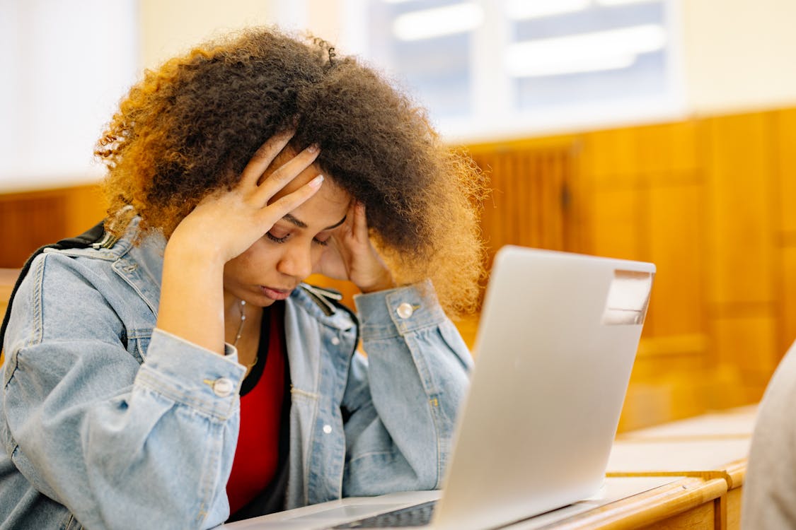 woman holding head with eyes closed while seated in front of laptop